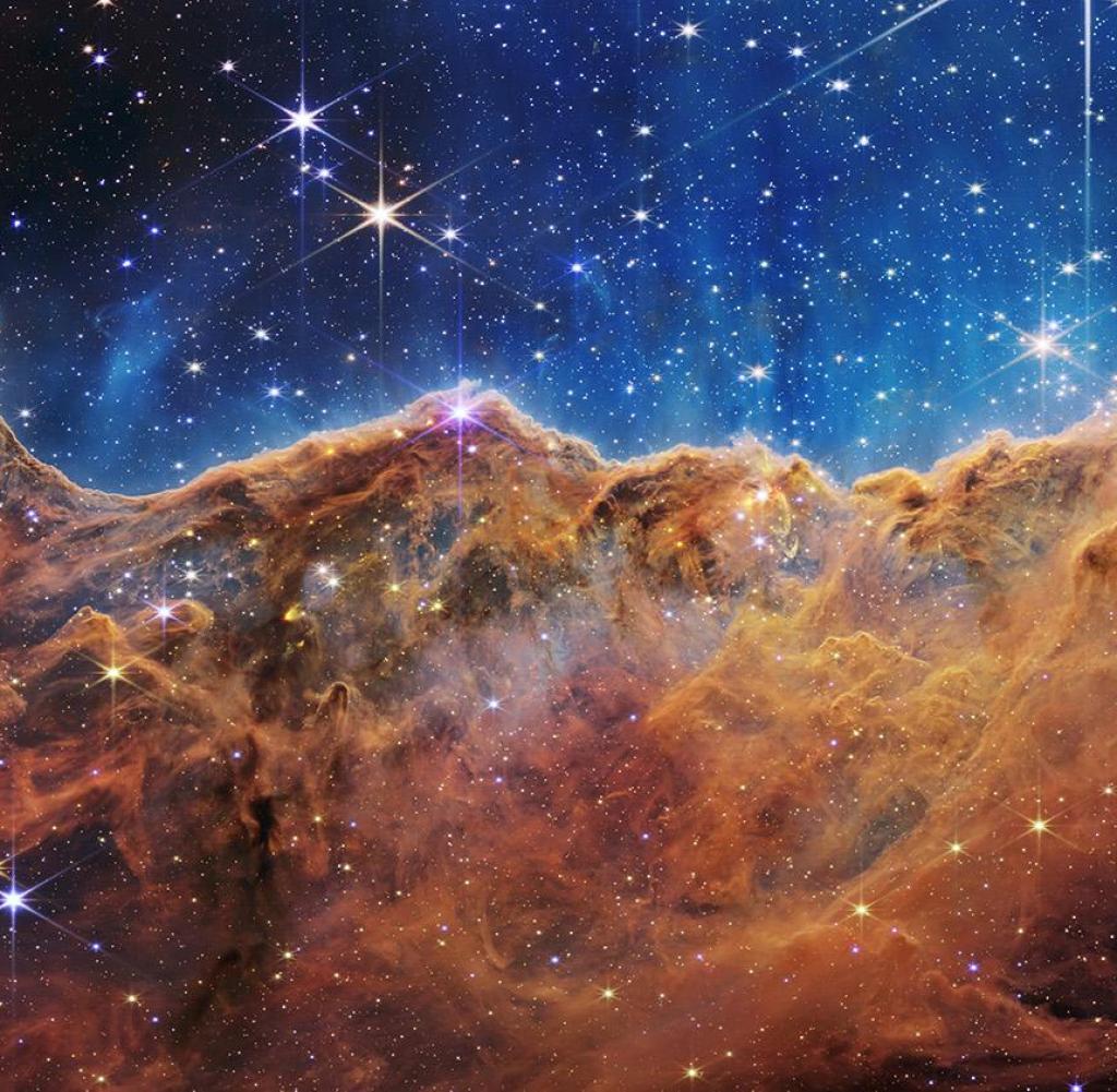 What looks a lot like rocky mountains on a moonlit evening is actually the edge of the nearby and young star-forming region NGC 3324 in the Carina Nebula.  Captured in infrared light by the Near Infrared Camera (NIRCam) on the NASA/ESA/CSA James Webb Space Telescope, this image reveals regions previously obscured by star births.  The region is called the Cosmic Slope, and it's actually the edge of a giant gas cavity within NGC 3324, about 7,600 light-years away.  The cavernous region of the nebula has been sculpted by intense ultraviolet radiation and stellar winds from young, extremely massive and hot stars in the center of the bubble, above the region shown in this image.  The high-energy radiation from these stars sculpts the nebula's wall by slowly eroding it.  With unparalleled accuracy and sensitivity, NIRCam unveils hundreds of previously hidden stars, and even many background galaxies.  Several notable features in this image are described below.  